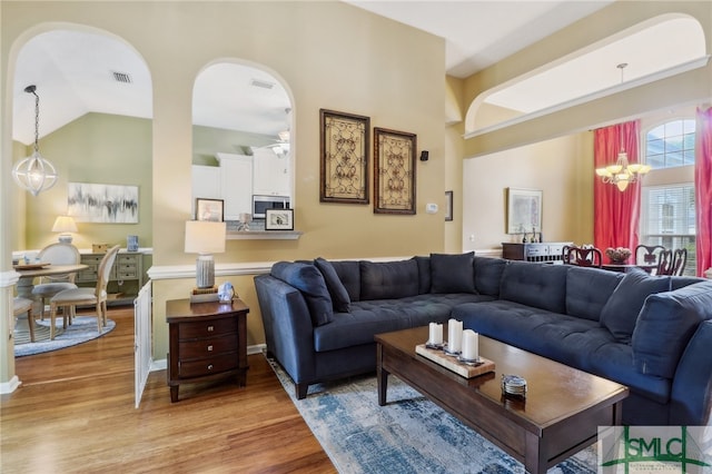 living room featuring light wood-type flooring, ceiling fan with notable chandelier, and lofted ceiling