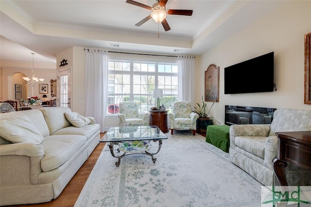 living room featuring ceiling fan with notable chandelier, a tray ceiling, wood finished floors, and crown molding