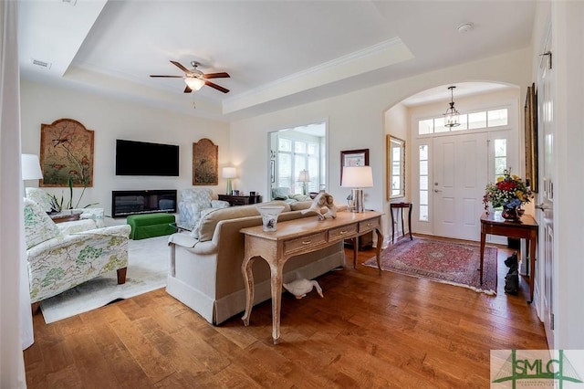 living room with hardwood / wood-style flooring, visible vents, a tray ceiling, and a ceiling fan