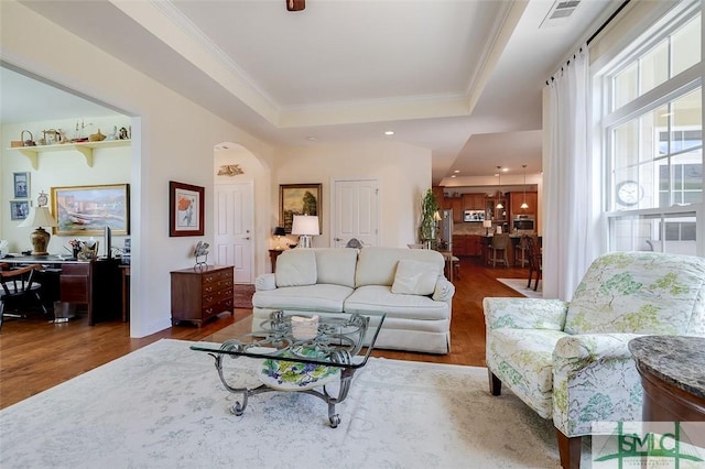 living room featuring visible vents, a raised ceiling, wood finished floors, and ornamental molding