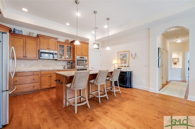 kitchen with arched walkways, decorative backsplash, light wood-style flooring, brown cabinets, and stainless steel appliances