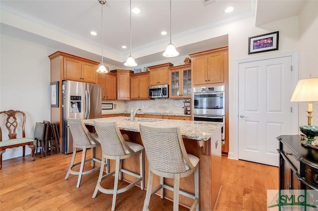 kitchen with a tray ceiling, a breakfast bar, appliances with stainless steel finishes, light wood-style floors, and a sink