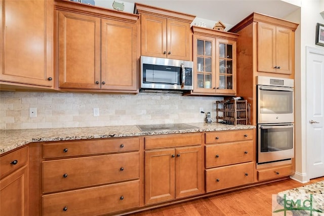 kitchen featuring light stone countertops, light wood finished floors, stainless steel appliances, and brown cabinetry