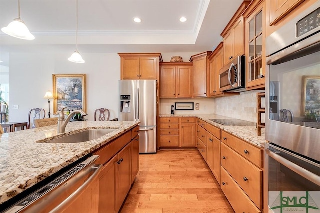 kitchen with light wood-style flooring, stainless steel appliances, a sink, hanging light fixtures, and a tray ceiling