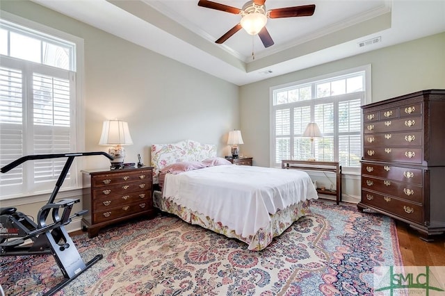 bedroom featuring ornamental molding, a raised ceiling, visible vents, and wood finished floors