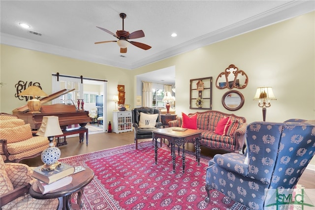 living room with a barn door, ceiling fan, wood-type flooring, and ornamental molding