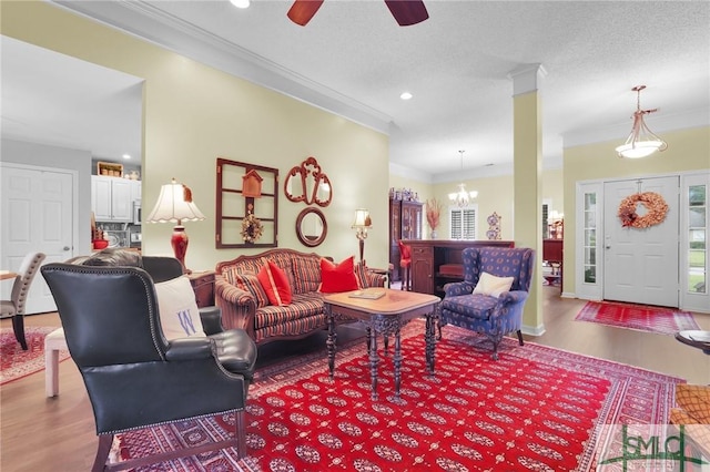 living area featuring a textured ceiling, ceiling fan with notable chandelier, crown molding, and wood finished floors