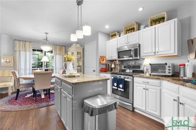 kitchen with pendant lighting, a center island, stainless steel appliances, dark wood-type flooring, and dark stone countertops