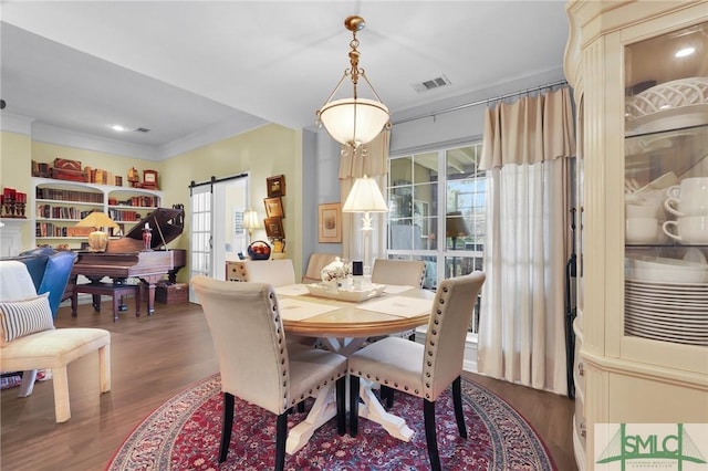 dining area with wood finished floors, visible vents, crown molding, and a barn door