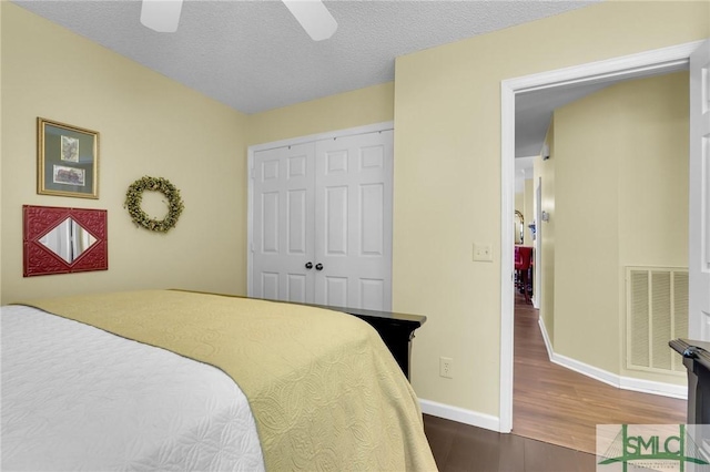 bedroom featuring a textured ceiling, wood finished floors, visible vents, baseboards, and a closet