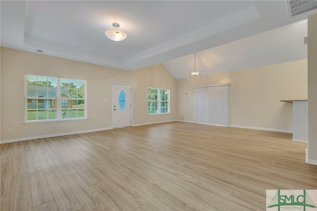 unfurnished living room with a tray ceiling, light hardwood / wood-style flooring, an inviting chandelier, and a healthy amount of sunlight