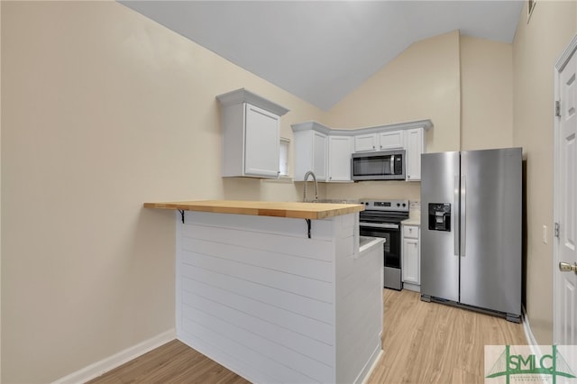 kitchen with wood counters, appliances with stainless steel finishes, light hardwood / wood-style floors, kitchen peninsula, and a kitchen bar