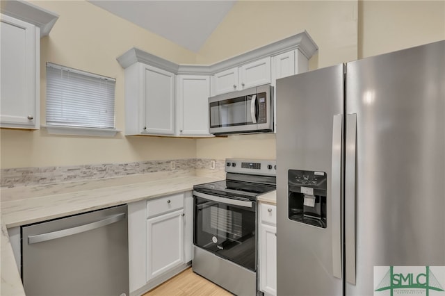 kitchen featuring lofted ceiling, light stone counters, appliances with stainless steel finishes, and white cabinets