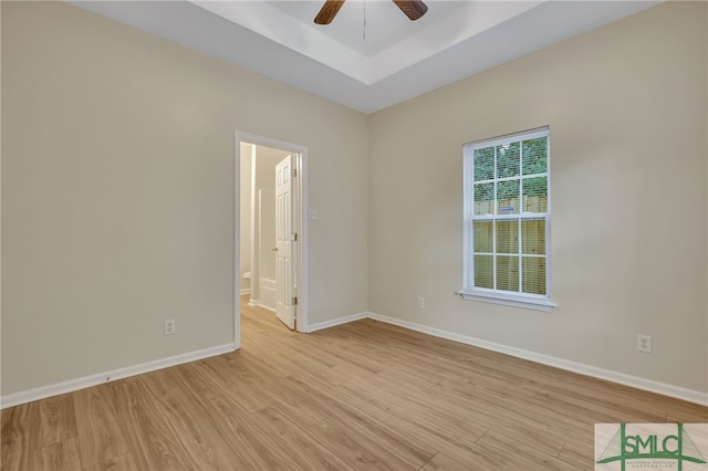 empty room featuring light wood-type flooring, a tray ceiling, and ceiling fan