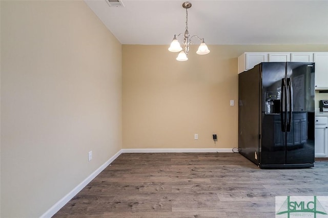 kitchen featuring an inviting chandelier, white cabinetry, hardwood / wood-style floors, black refrigerator with ice dispenser, and hanging light fixtures