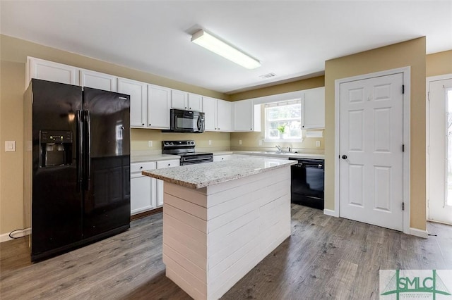 kitchen with light stone countertops, white cabinets, black appliances, a kitchen island, and light wood-type flooring