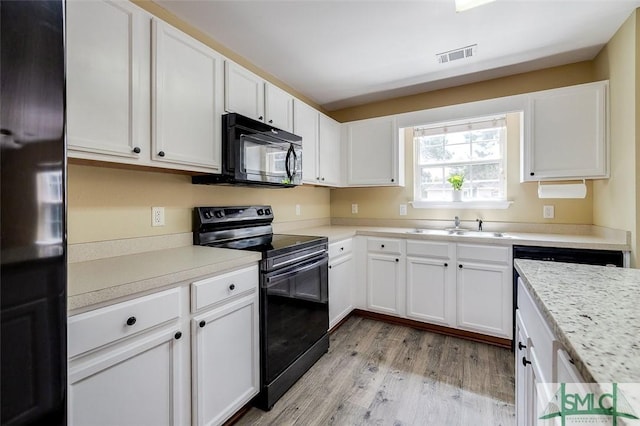 kitchen with light hardwood / wood-style floors, black appliances, sink, light stone countertops, and white cabinets