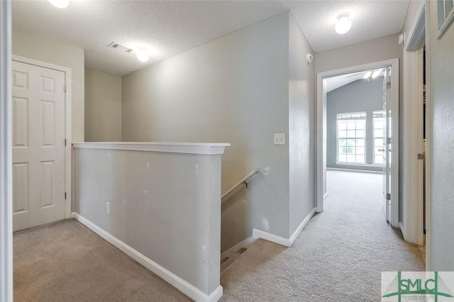 corridor featuring a textured ceiling, lofted ceiling, and light colored carpet