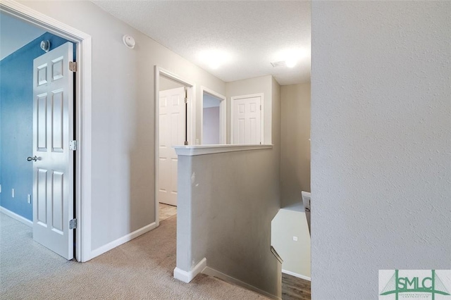 corridor with light carpet and a textured ceiling