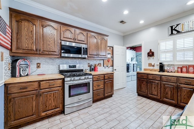 kitchen with backsplash, stainless steel appliances, washing machine and dryer, and ornamental molding