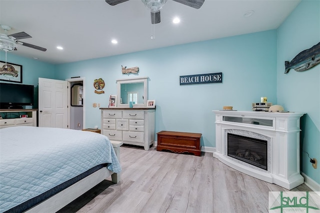 bedroom featuring light wood-type flooring, ceiling fan, and a fireplace