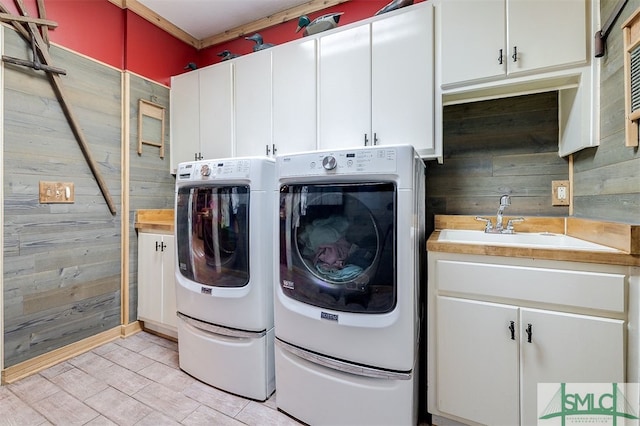 laundry area featuring wood walls, sink, cabinets, and washer and dryer