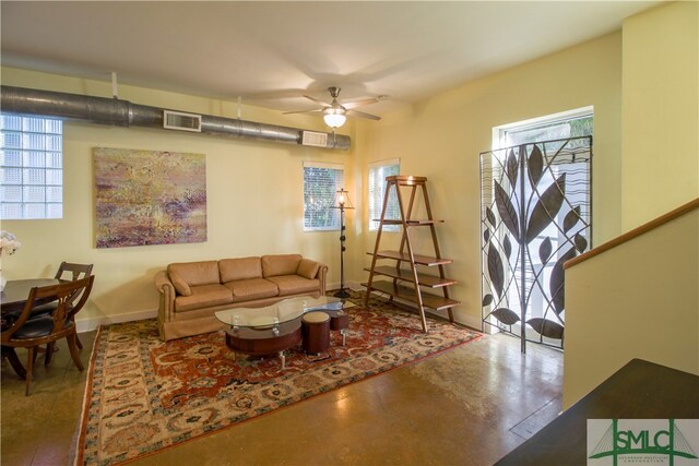 living room featuring a wealth of natural light, concrete flooring, and ceiling fan