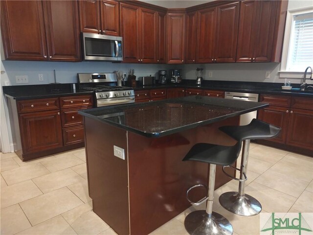 kitchen with sink, light tile patterned floors, a kitchen island, a kitchen bar, and stainless steel appliances