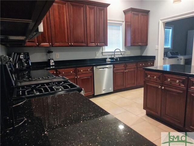 kitchen featuring washer and clothes dryer, dark stone counters, sink, stainless steel dishwasher, and light tile patterned floors