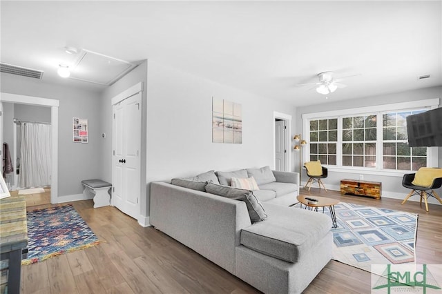 living area with attic access, ceiling fan, wood finished floors, and baseboards