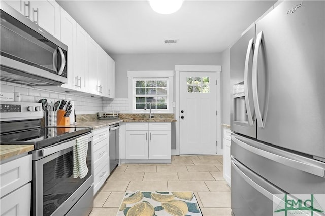 kitchen with stainless steel appliances, white cabinets, backsplash, and light tile patterned flooring
