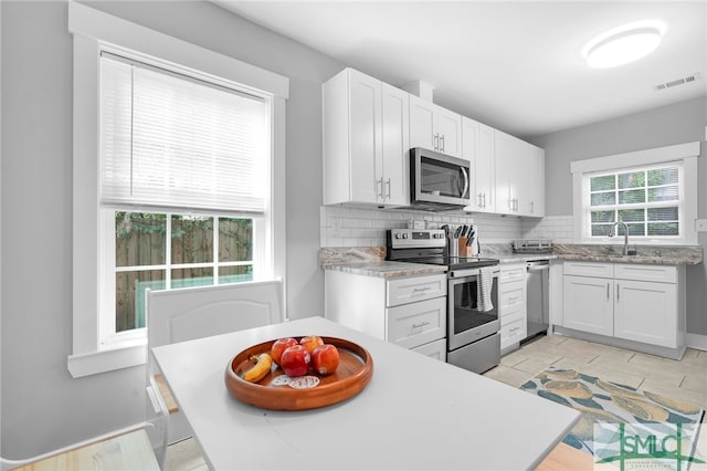 kitchen with appliances with stainless steel finishes, sink, decorative backsplash, white cabinets, and light tile patterned flooring