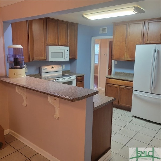 kitchen featuring white appliances, light tile patterned floors, a breakfast bar area, and kitchen peninsula