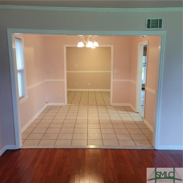 empty room with crown molding, a chandelier, and light hardwood / wood-style floors