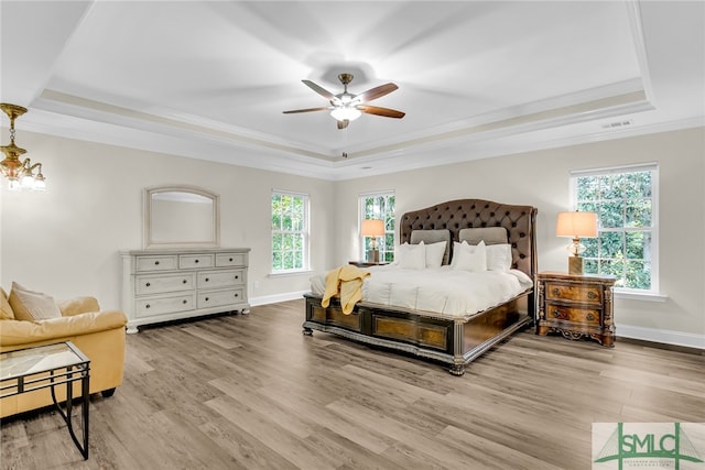 bedroom with ceiling fan with notable chandelier, wood-type flooring, a tray ceiling, and multiple windows