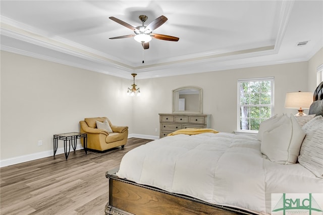 bedroom featuring light wood-type flooring, ceiling fan, a raised ceiling, and crown molding