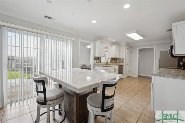 kitchen featuring a healthy amount of sunlight, a kitchen bar, light tile patterned floors, and white cabinets