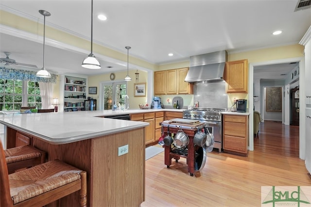 kitchen with high end stainless steel range, wall chimney exhaust hood, a healthy amount of sunlight, and a breakfast bar area