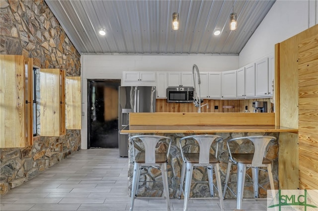 kitchen featuring wooden ceiling, appliances with stainless steel finishes, a breakfast bar, white cabinetry, and lofted ceiling