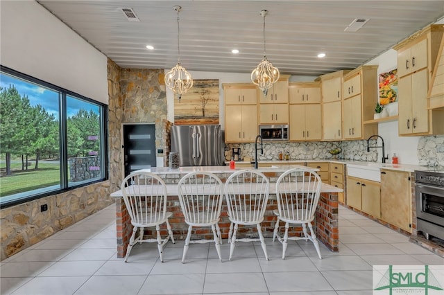 kitchen featuring a center island with sink, pendant lighting, a notable chandelier, appliances with stainless steel finishes, and light brown cabinets