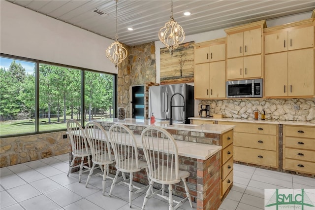 kitchen featuring a healthy amount of sunlight, a chandelier, appliances with stainless steel finishes, a center island with sink, and light brown cabinets