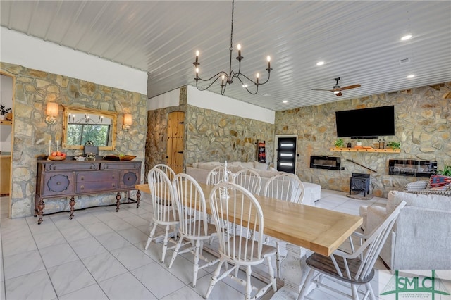 dining space with ceiling fan with notable chandelier, a wood stove, a stone fireplace, wood ceiling, and light tile patterned flooring