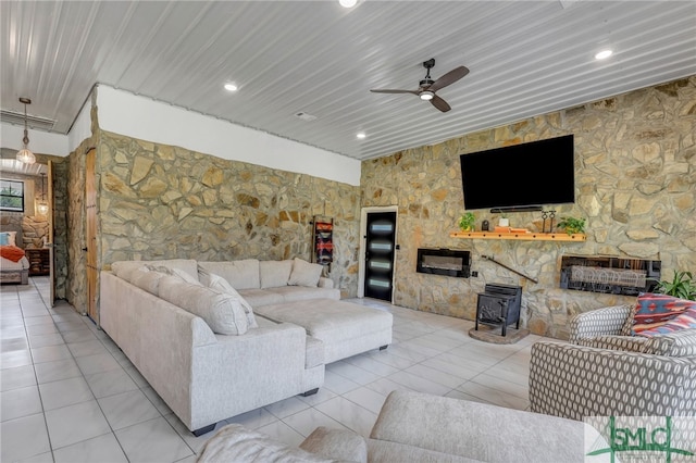 living room featuring a wood stove, ceiling fan, light tile patterned floors, and a fireplace