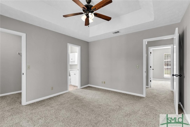 unfurnished bedroom with baseboards, visible vents, a tray ceiling, a spacious closet, and light carpet