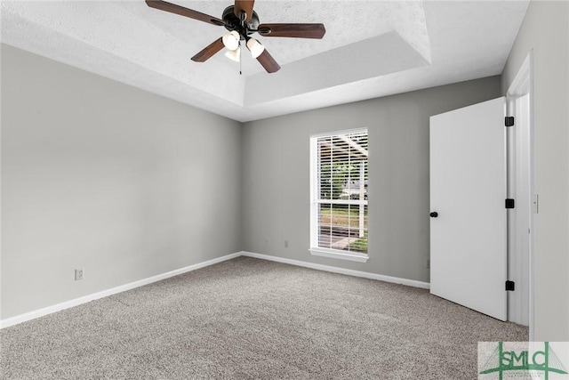 empty room featuring a tray ceiling, baseboards, a textured ceiling, and carpet flooring