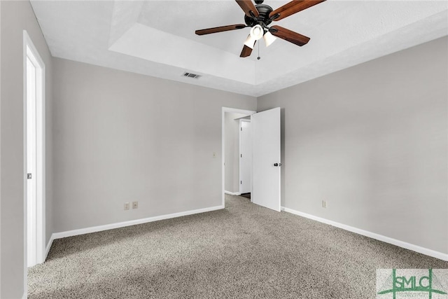 unfurnished bedroom with a ceiling fan, carpet, visible vents, baseboards, and a tray ceiling