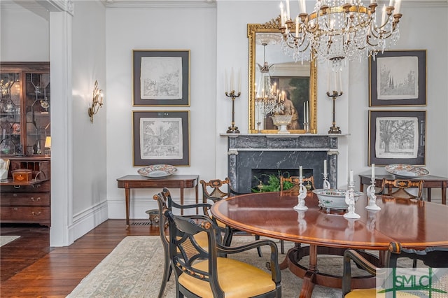 dining area featuring dark wood-type flooring, a chandelier, a high end fireplace, and ornamental molding