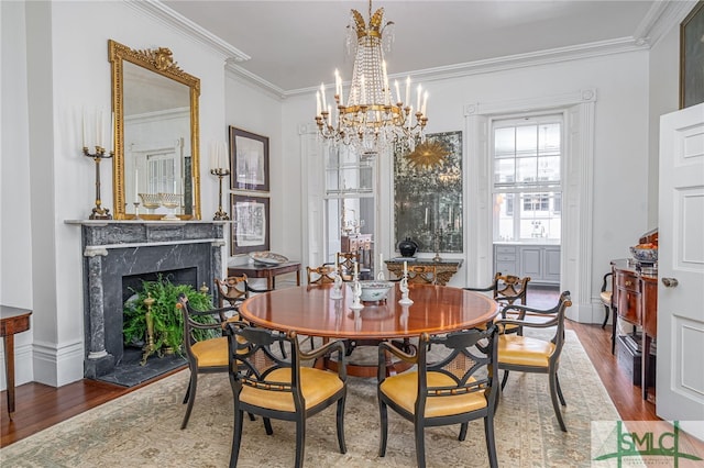 dining room featuring wood-type flooring, ornamental molding, an inviting chandelier, and a premium fireplace