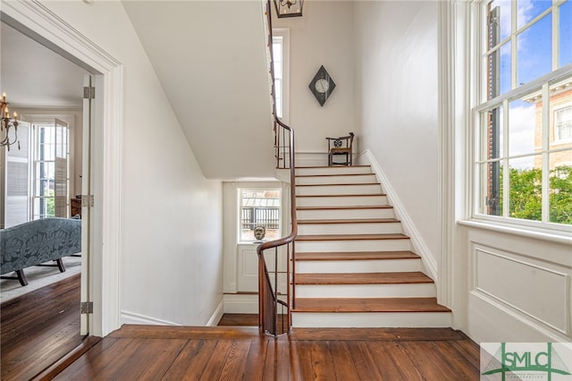 staircase with a healthy amount of sunlight, a notable chandelier, and hardwood / wood-style floors