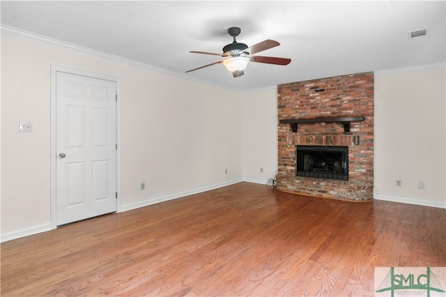 unfurnished living room featuring hardwood / wood-style floors, ceiling fan, crown molding, and a brick fireplace